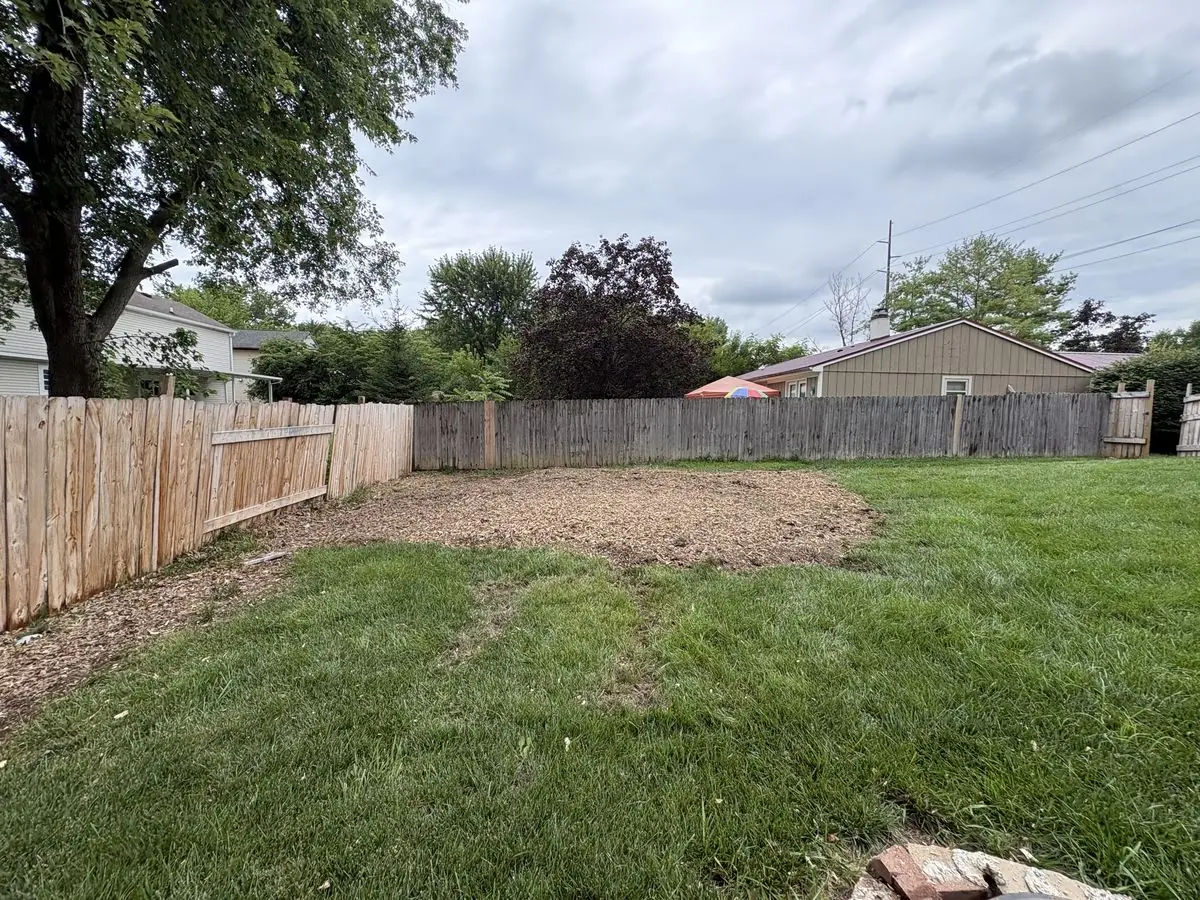 Same back yard after log removal and stump grinding — lawn cleared with a level bed of grindings along the fence