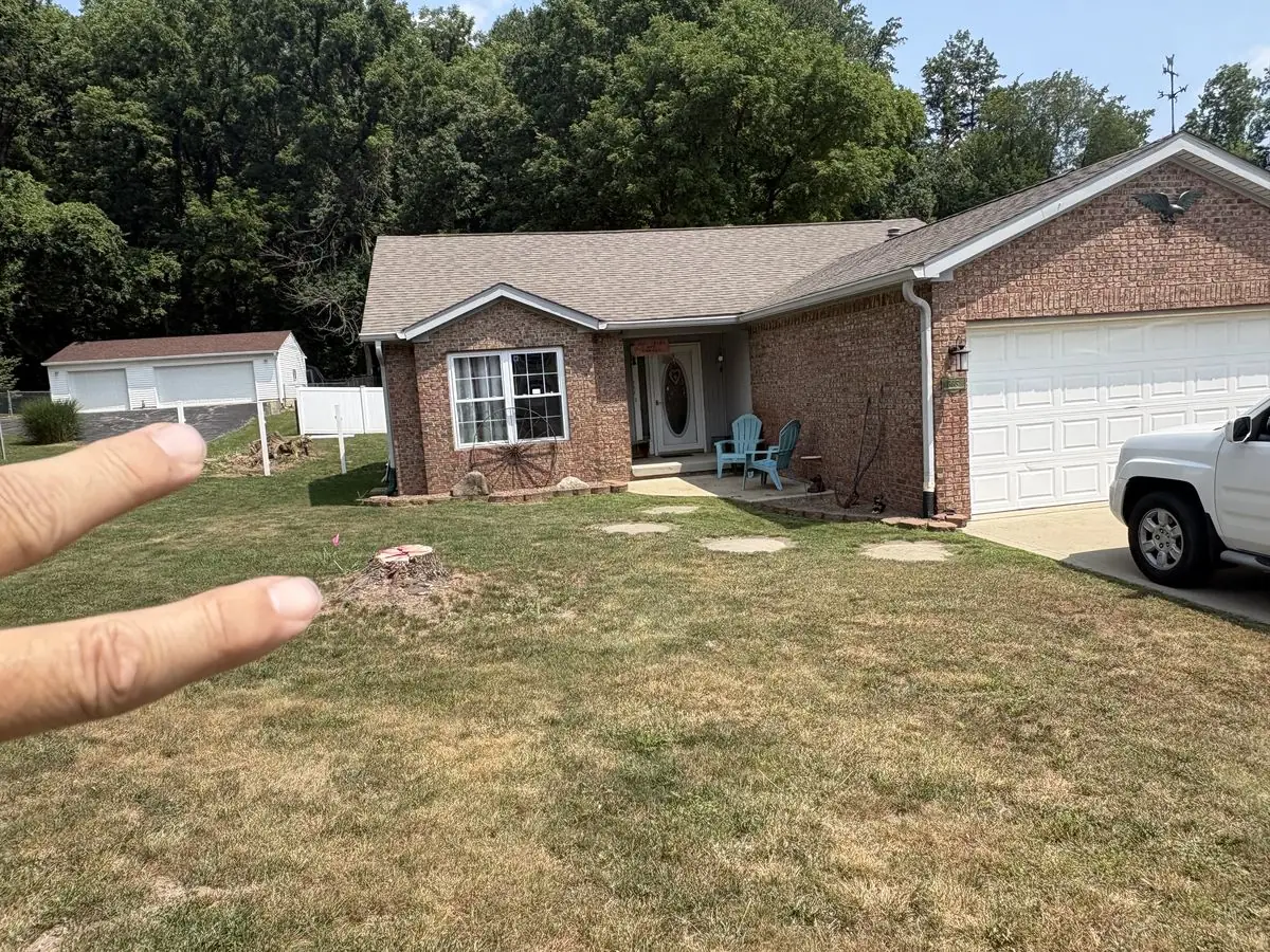 Fresh-cut tree stump in the front lawn of a brick home before stump grinding in South Central Indiana